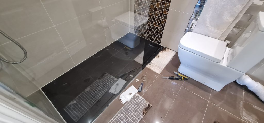 Bathroom repair showing floor tiles removed near shower area during leak investigation and repair in London